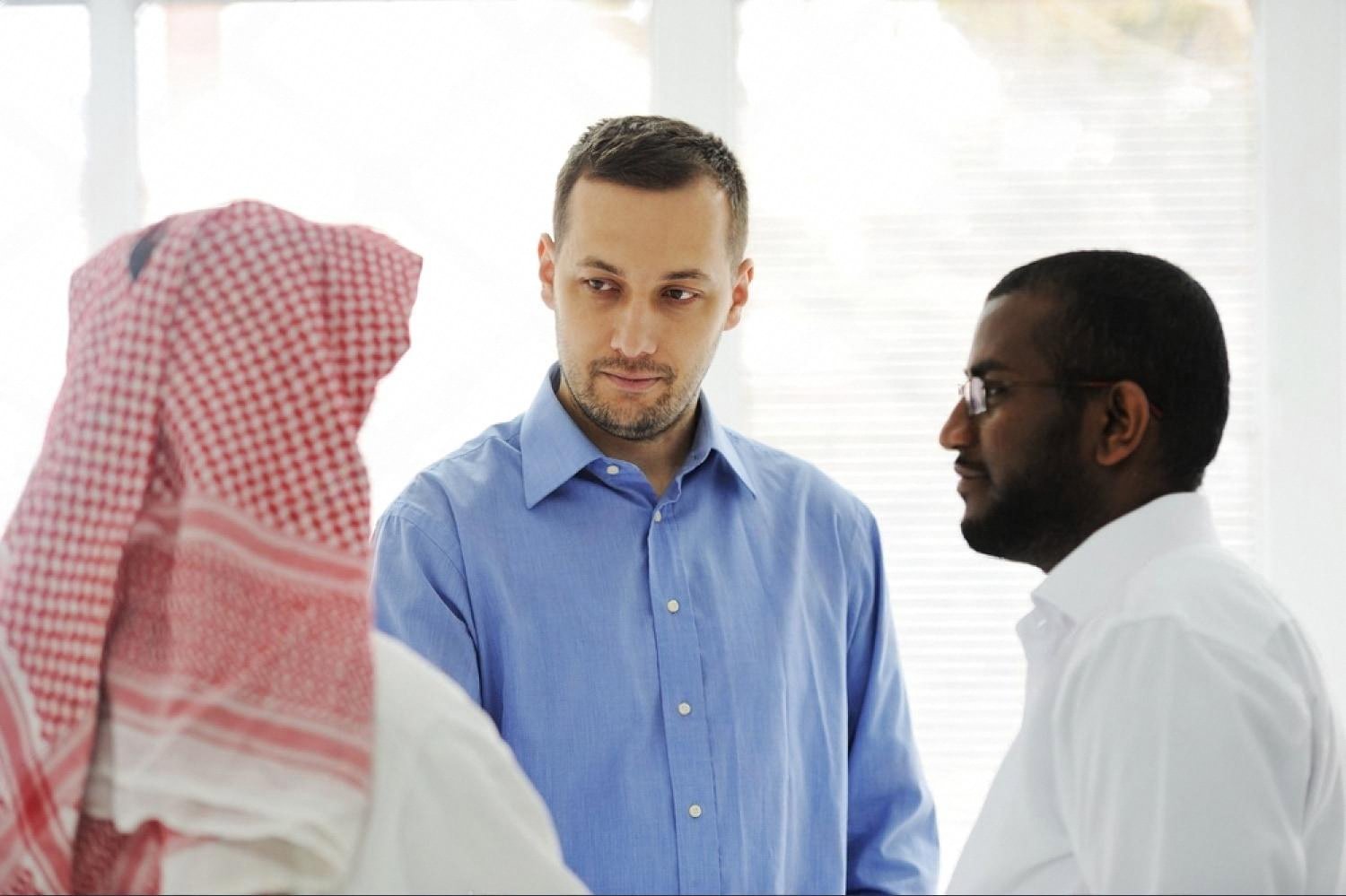 Two businessmen in Dubai discussing a partnership with a colleague in traditional Gulf dress